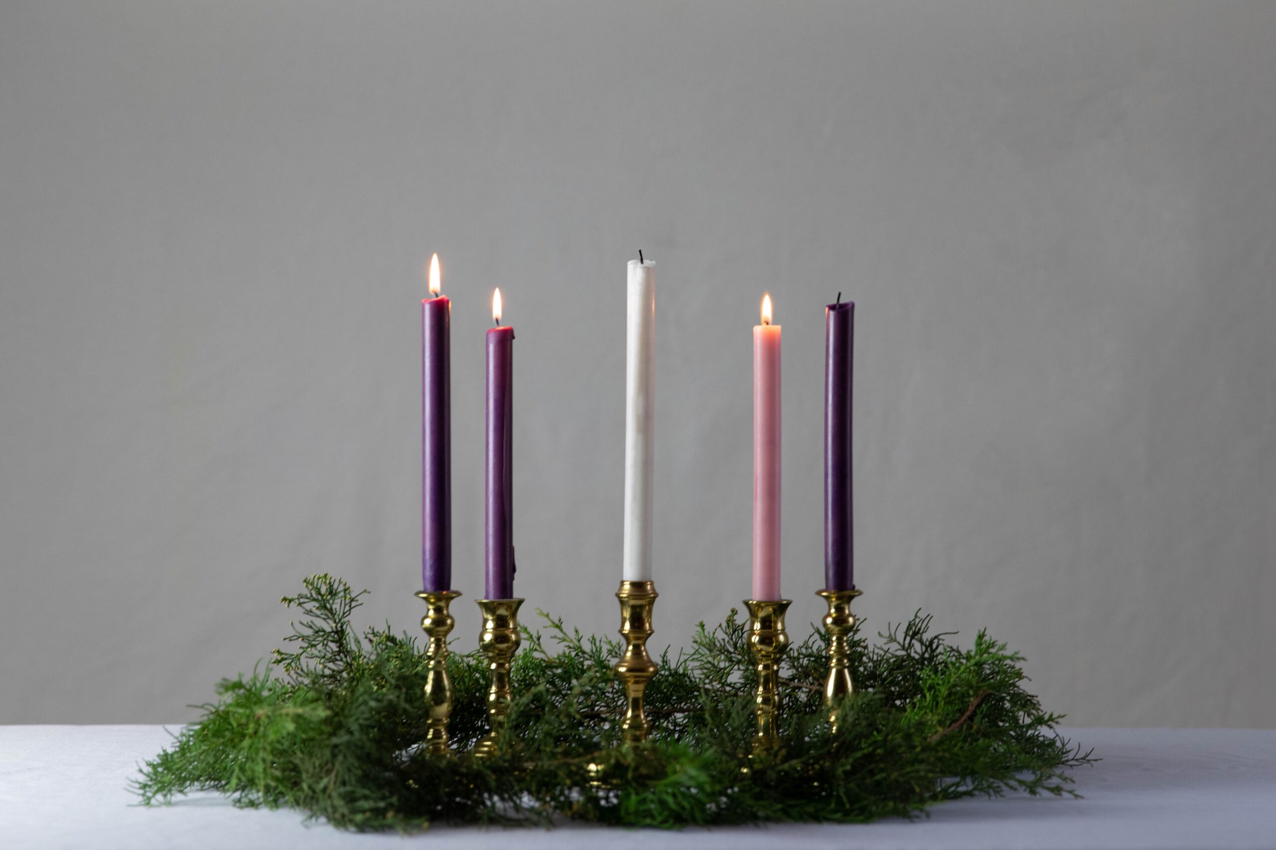 Advent wreath with greenry Three candles are lit, and two are not, including one tall white one in the center.