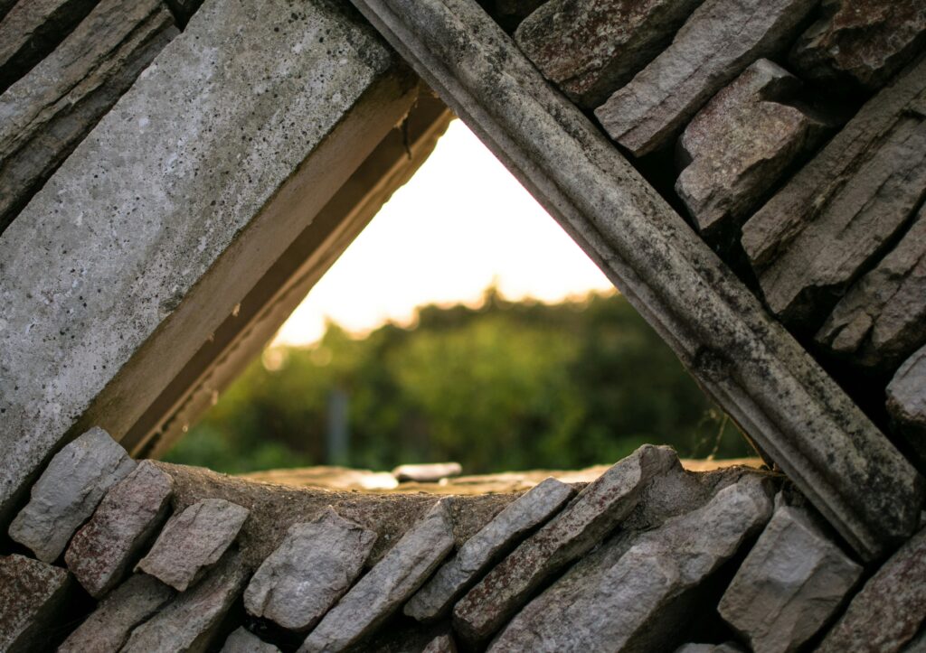 Greenery visible through a triangular hole in a rustic rock wall.