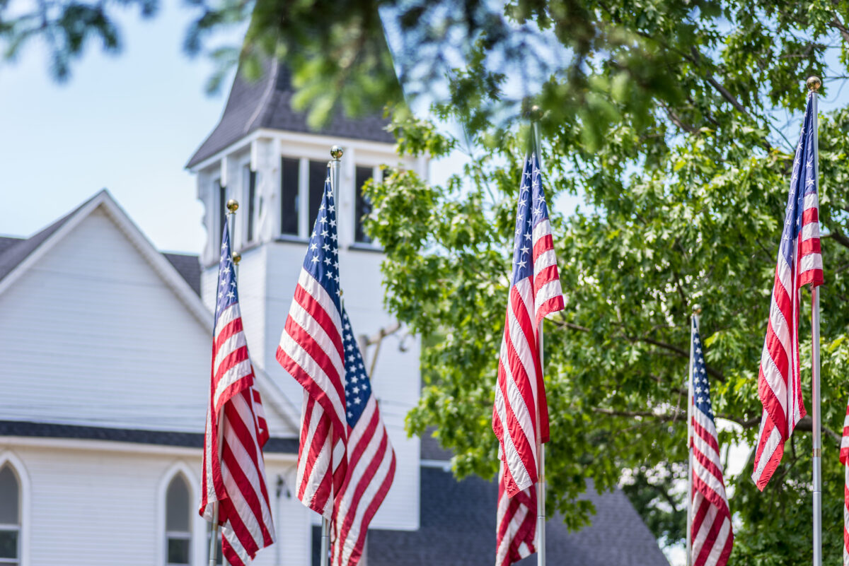 US flags in front of a church steeple.