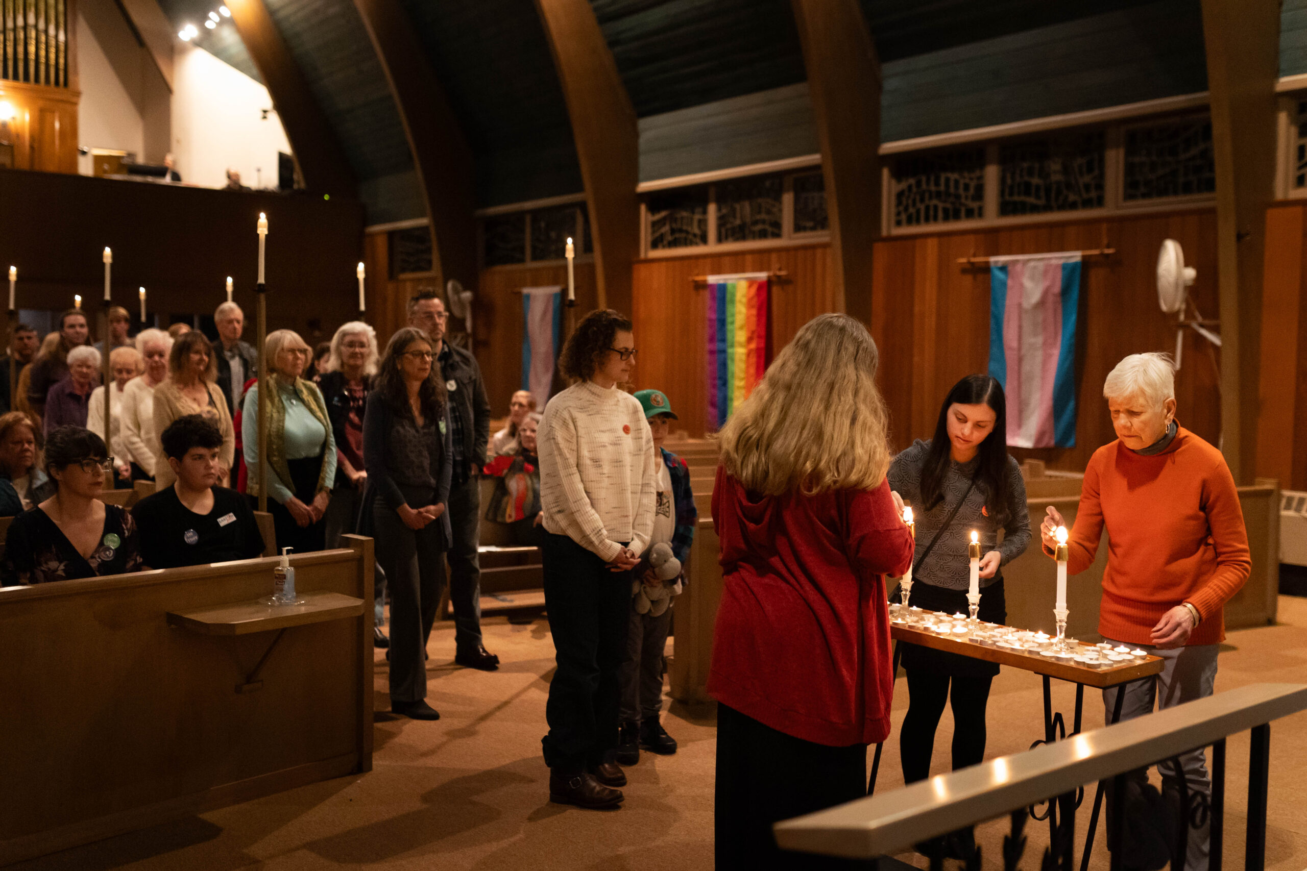 Image showing people lining up to light candles in the Holy Trinity sanctuary, with transgender and rainbow flags visible in background.